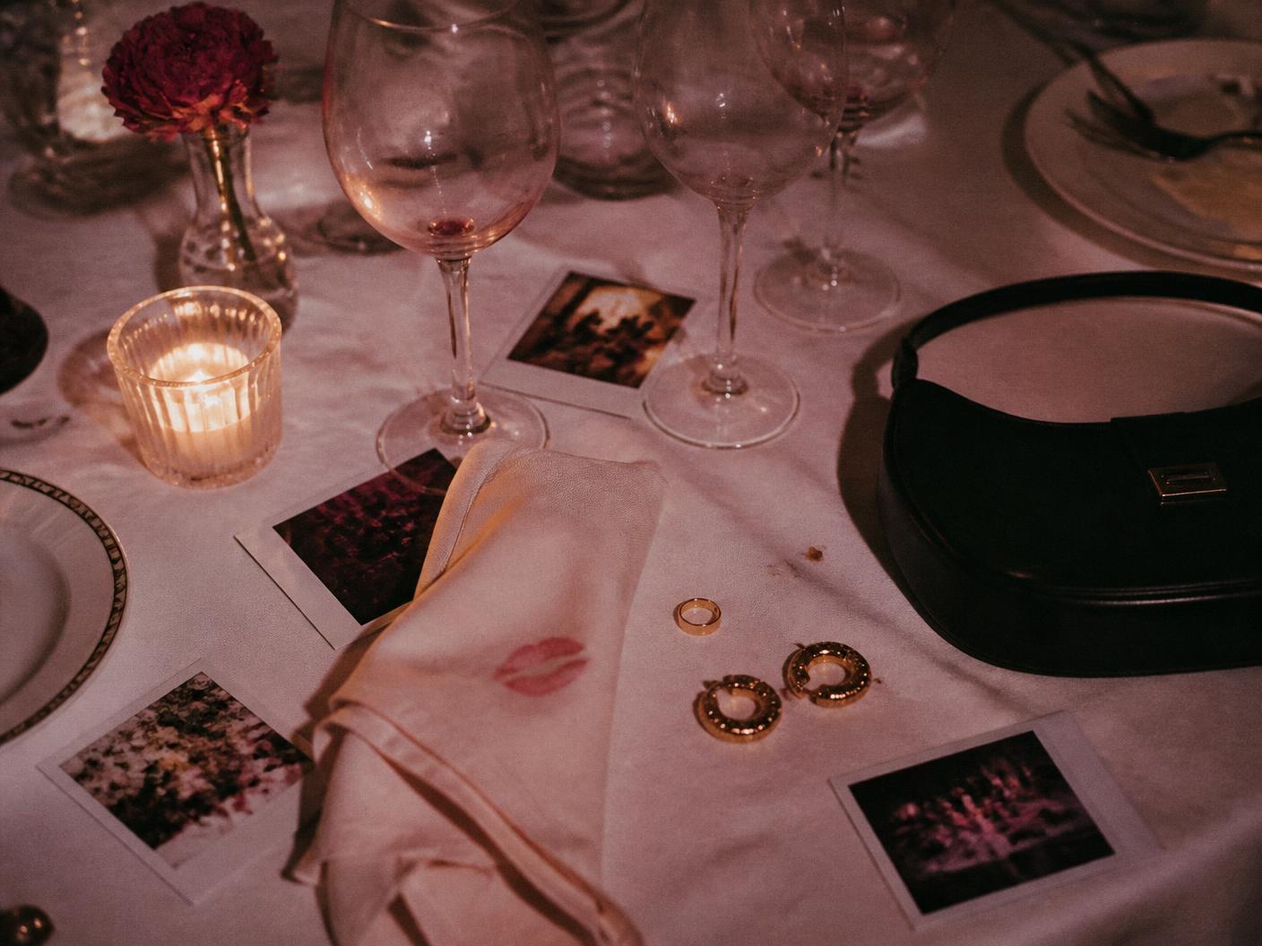 Tavolo dopo una cena: bicchieri, rossetto su un tovagliolo, polaroid e gioielli in oro